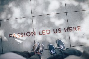 Two people's feet on a sidewalk with the words "passion led us here" written on it